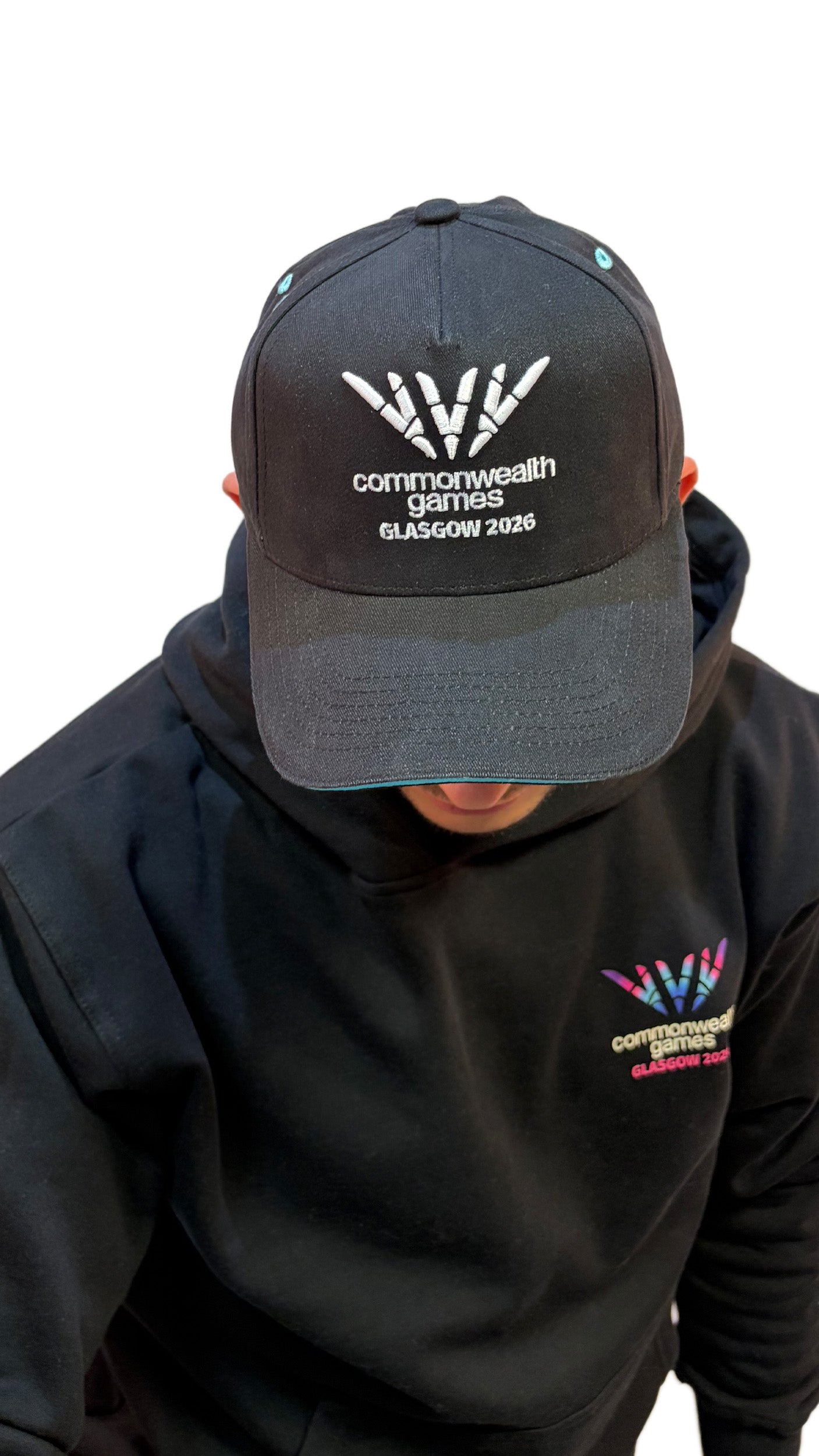 Front View of man wearing black baseball cap with teal sandwich peak and white 3D embroidered Glasgow 2026 logo.
