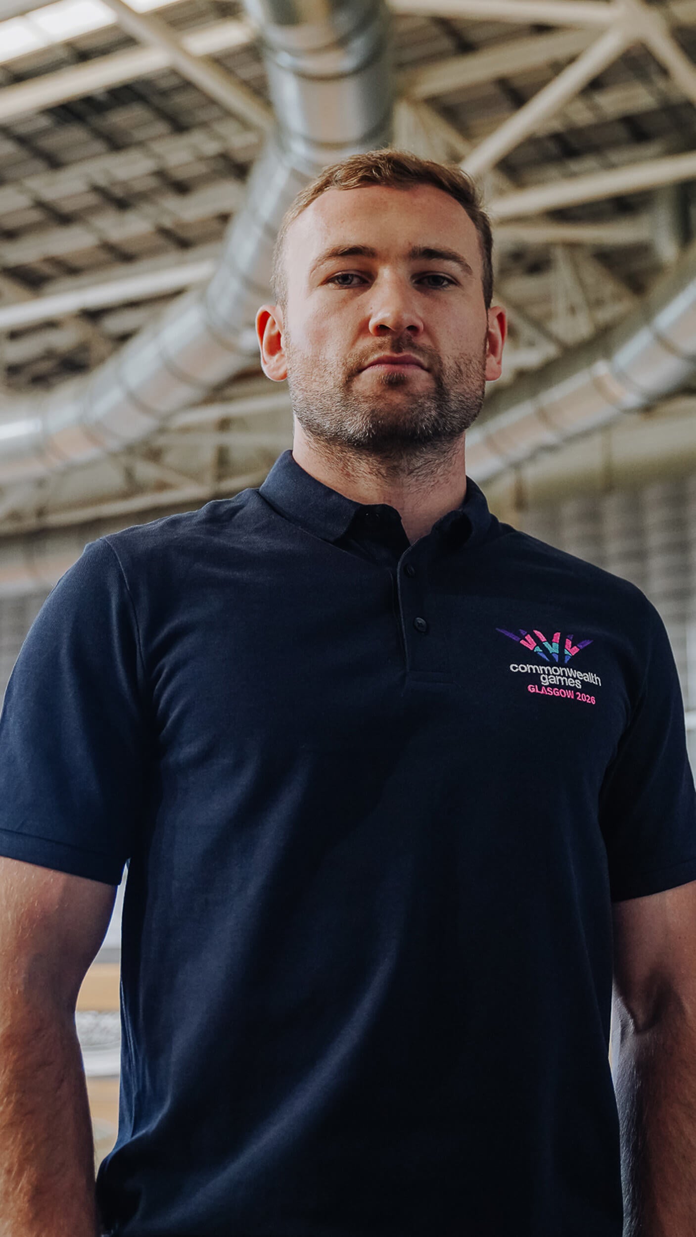 Man wearing navy polo shirt with full colour embroidered Glasgow 2026 logo.