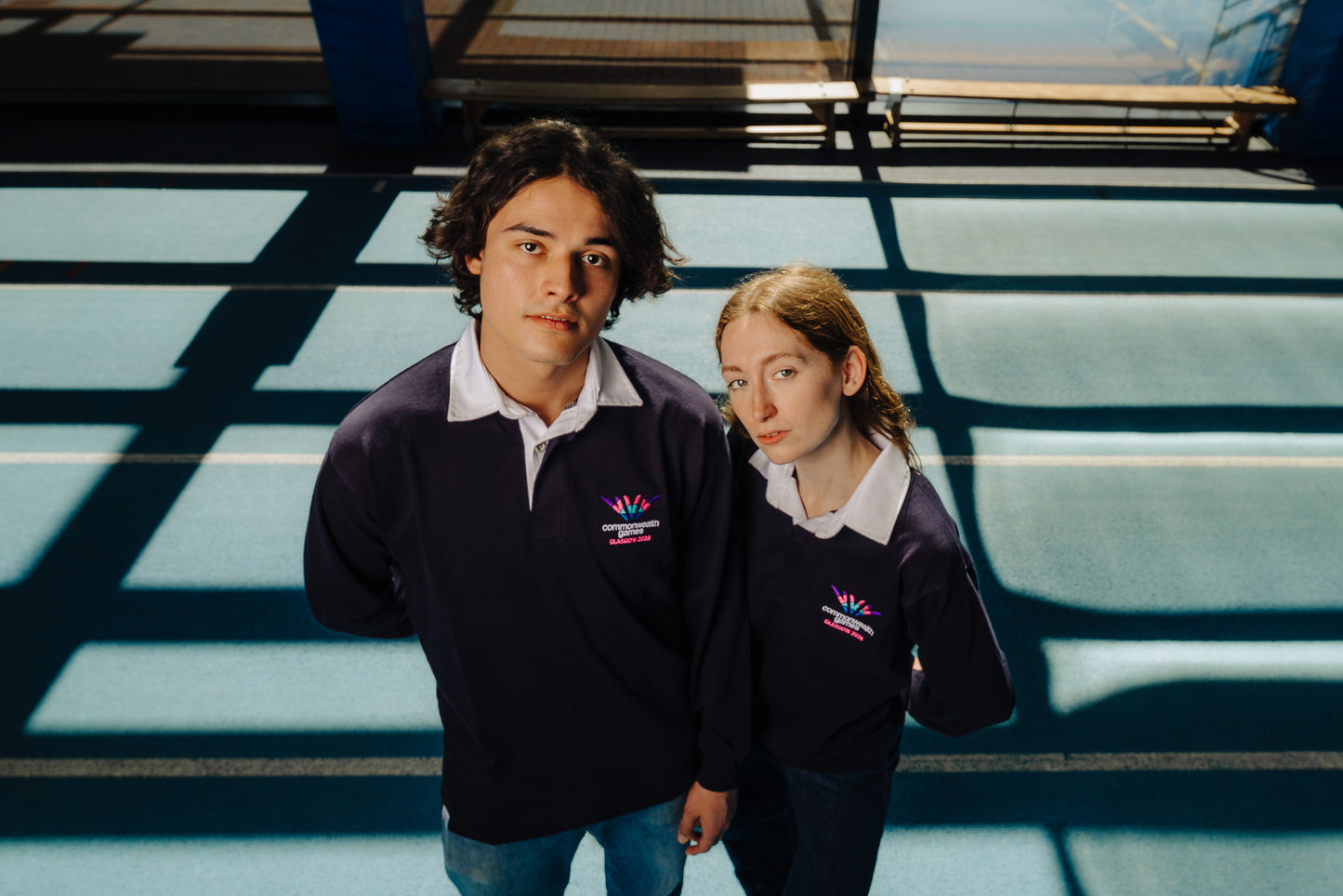 Man and woman wearing Glasgow 2026 navy rugby tops with embroidered full colour logo.