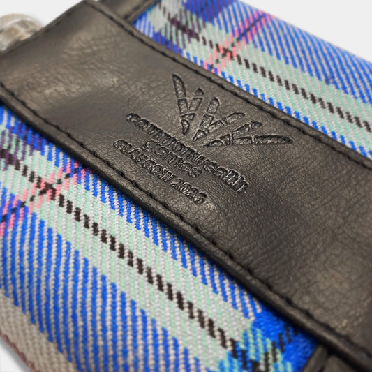 Close up view of Glasgow 2026 Tartan Hip Flask on grey background showing debossed logo detail