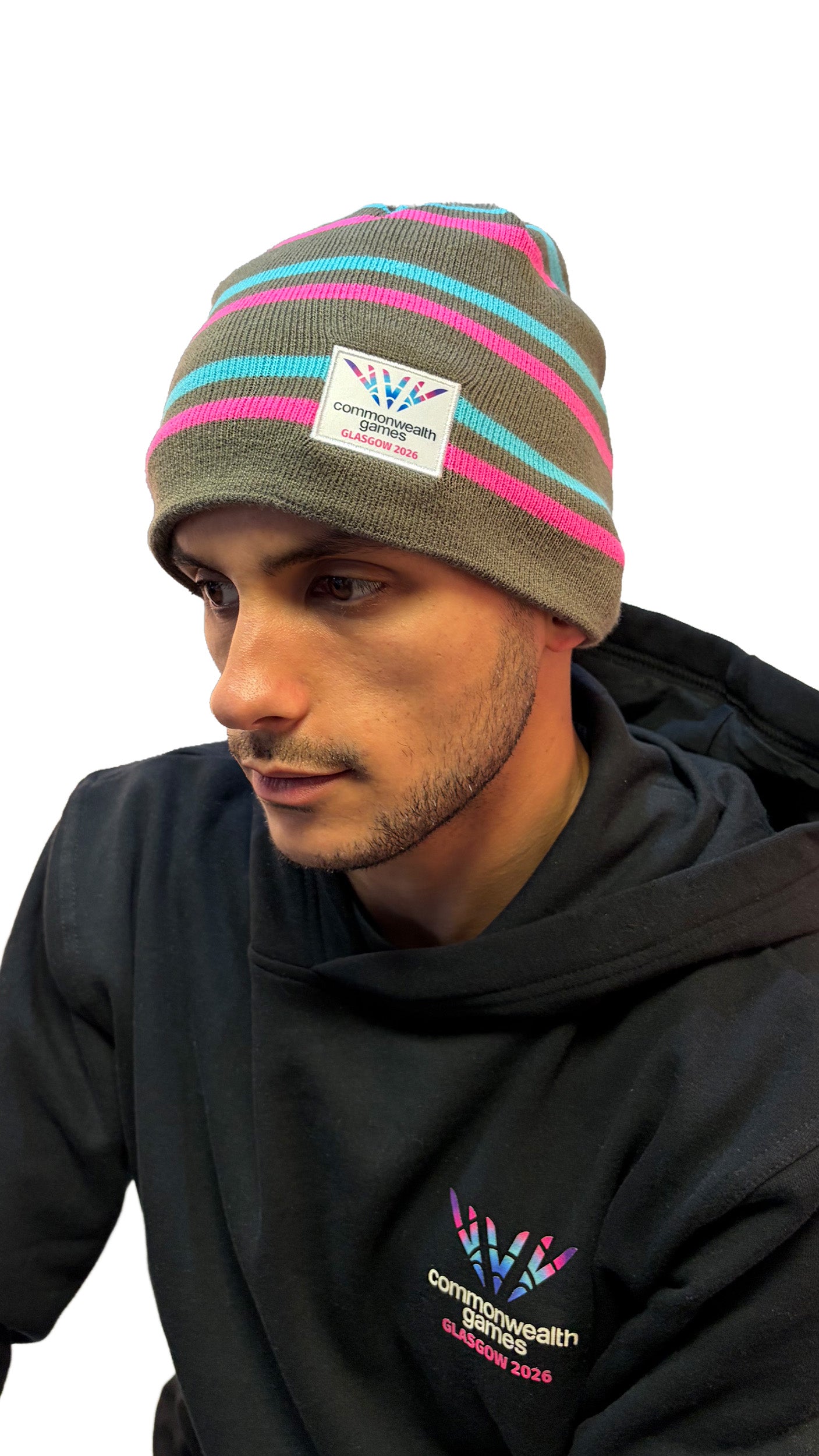 Man wearing grey beanie with pink and blue stripes and Glasgow 2026 logo.