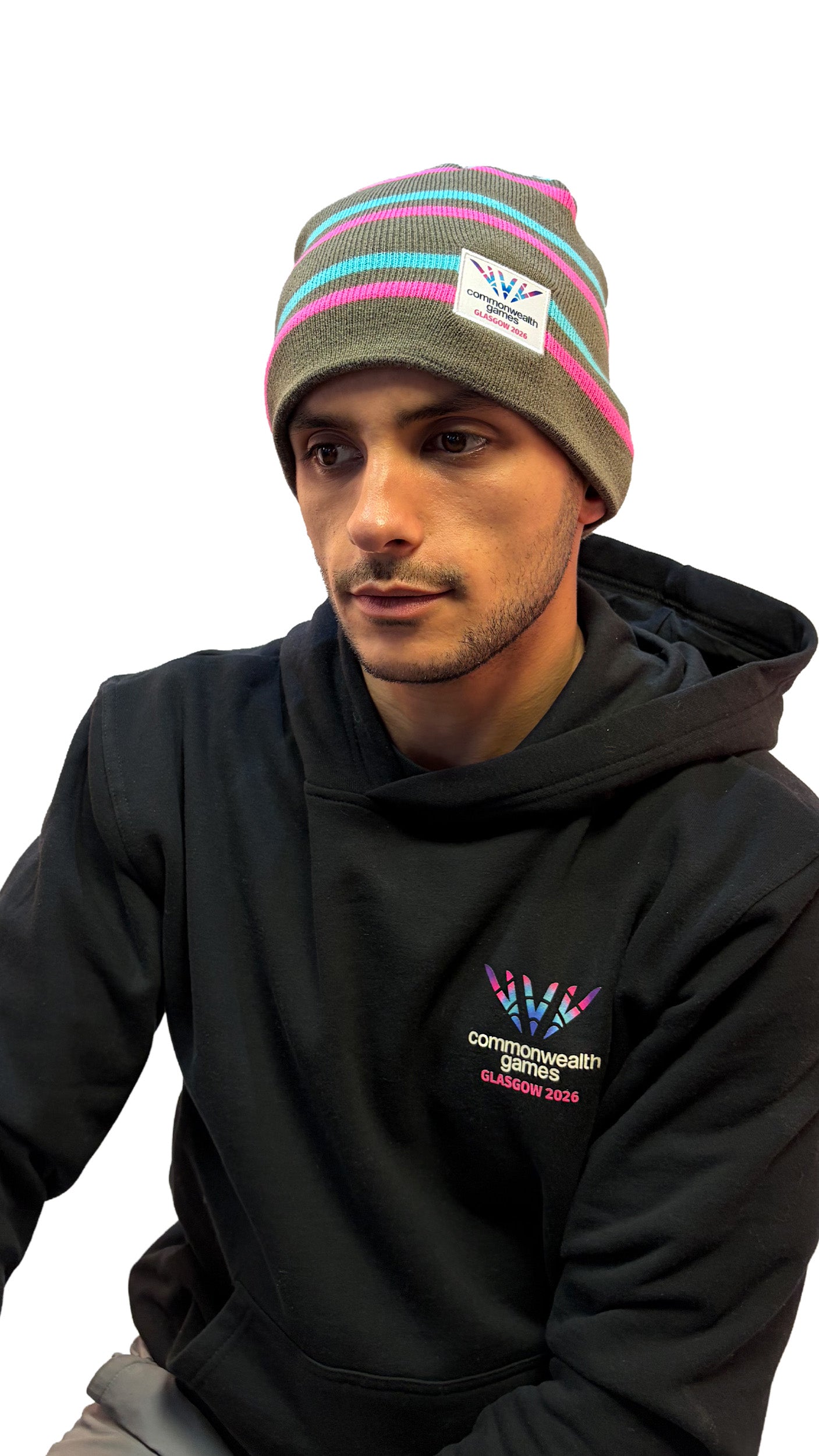 Man wearing grey beanie with pink and blue stripes and Glasgow 2026 logo.
