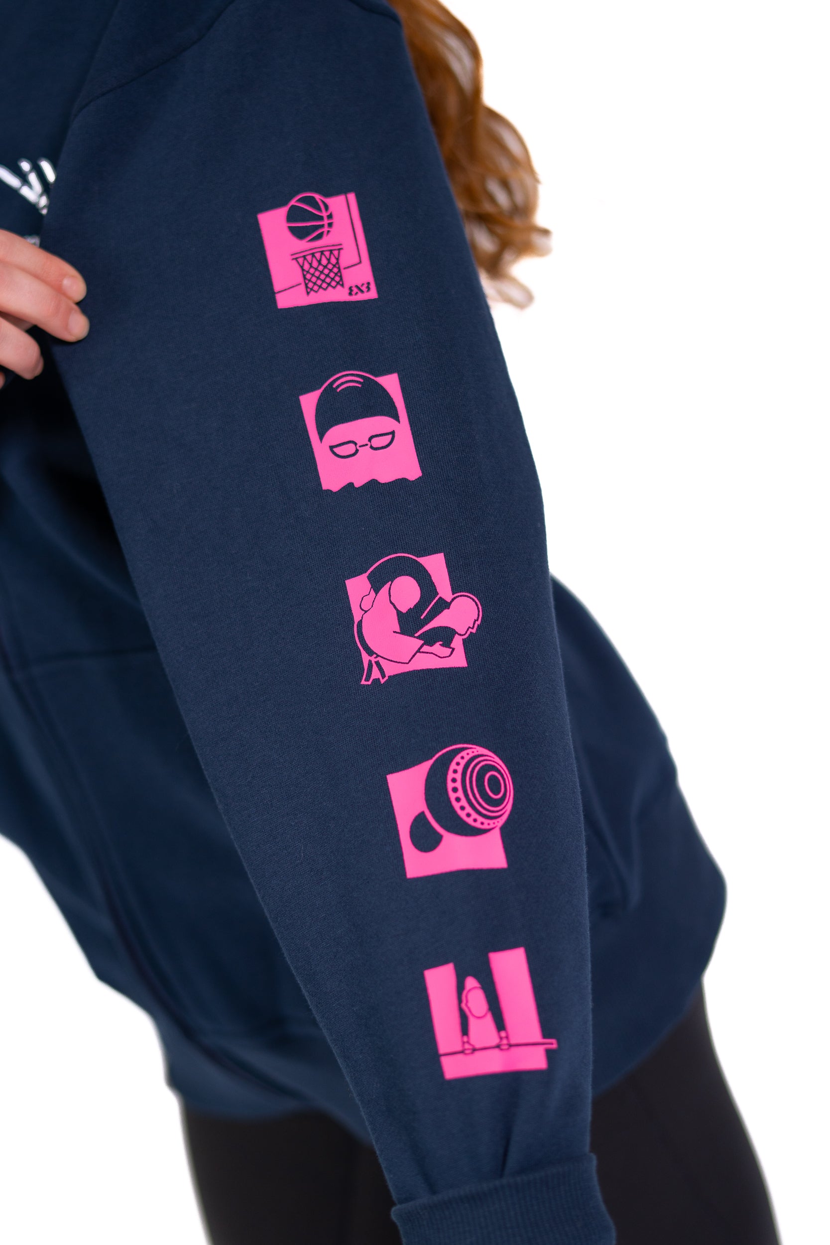 Close up of woman wearing contrast navy/pink Glasgow 2026 Pictograms hoodie showing sport pictograms on sleeve.