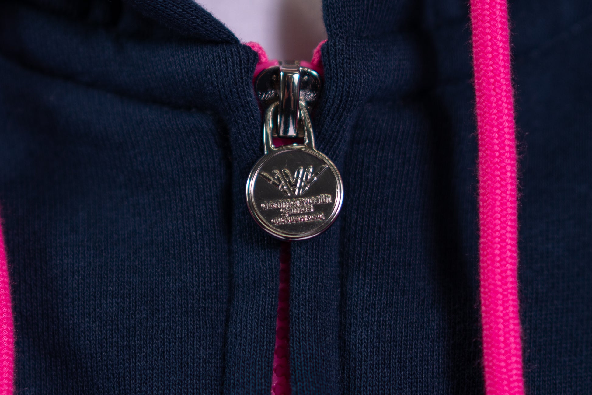 Close up of woman wearing contrast navy/pink Glasgow 2026 Pictograms hoodie showing custom Glasgow 2026 logo zip pull.
