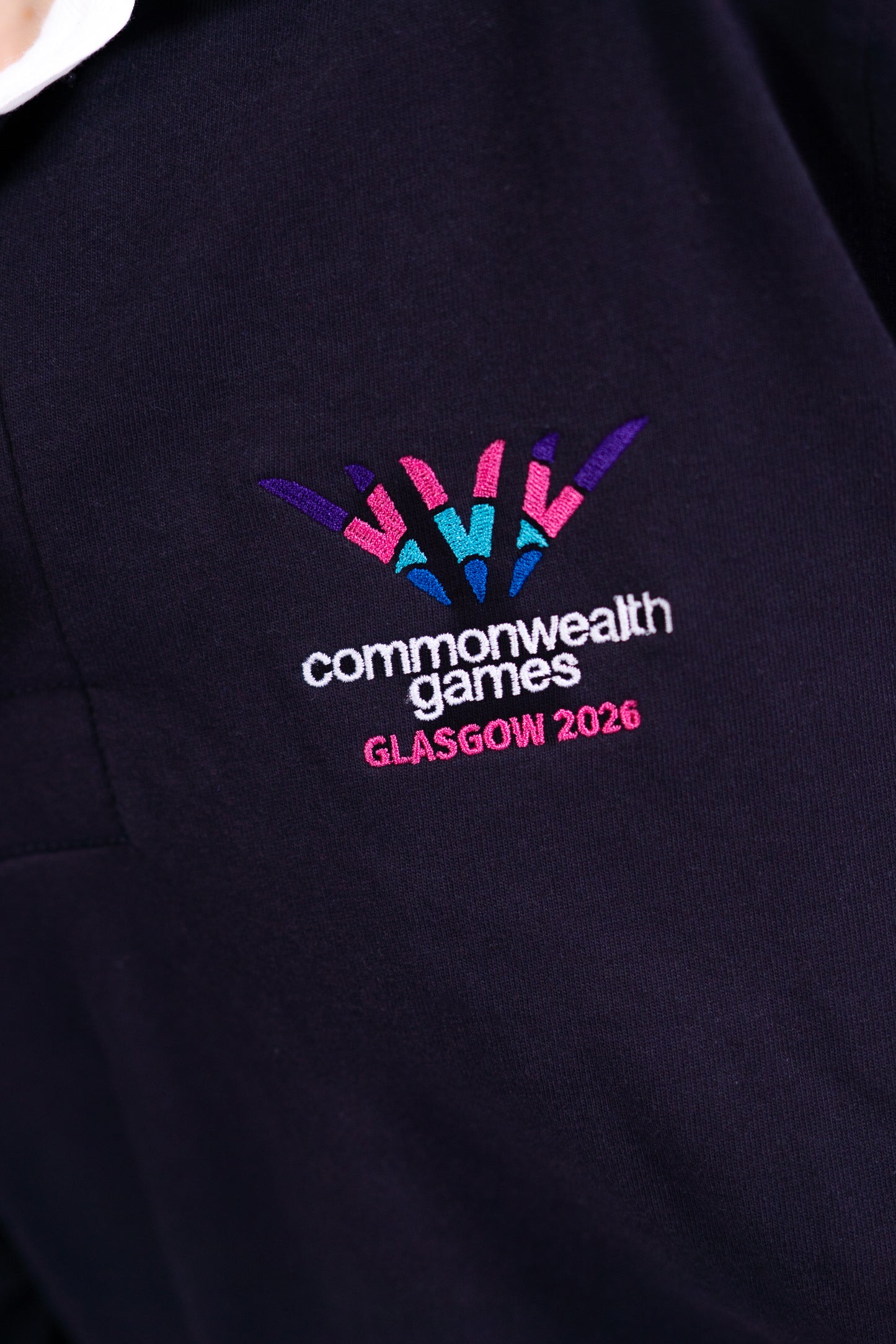 Close up navy Glasgow 2026 logo rugby top with white collar showing logo embroidery.