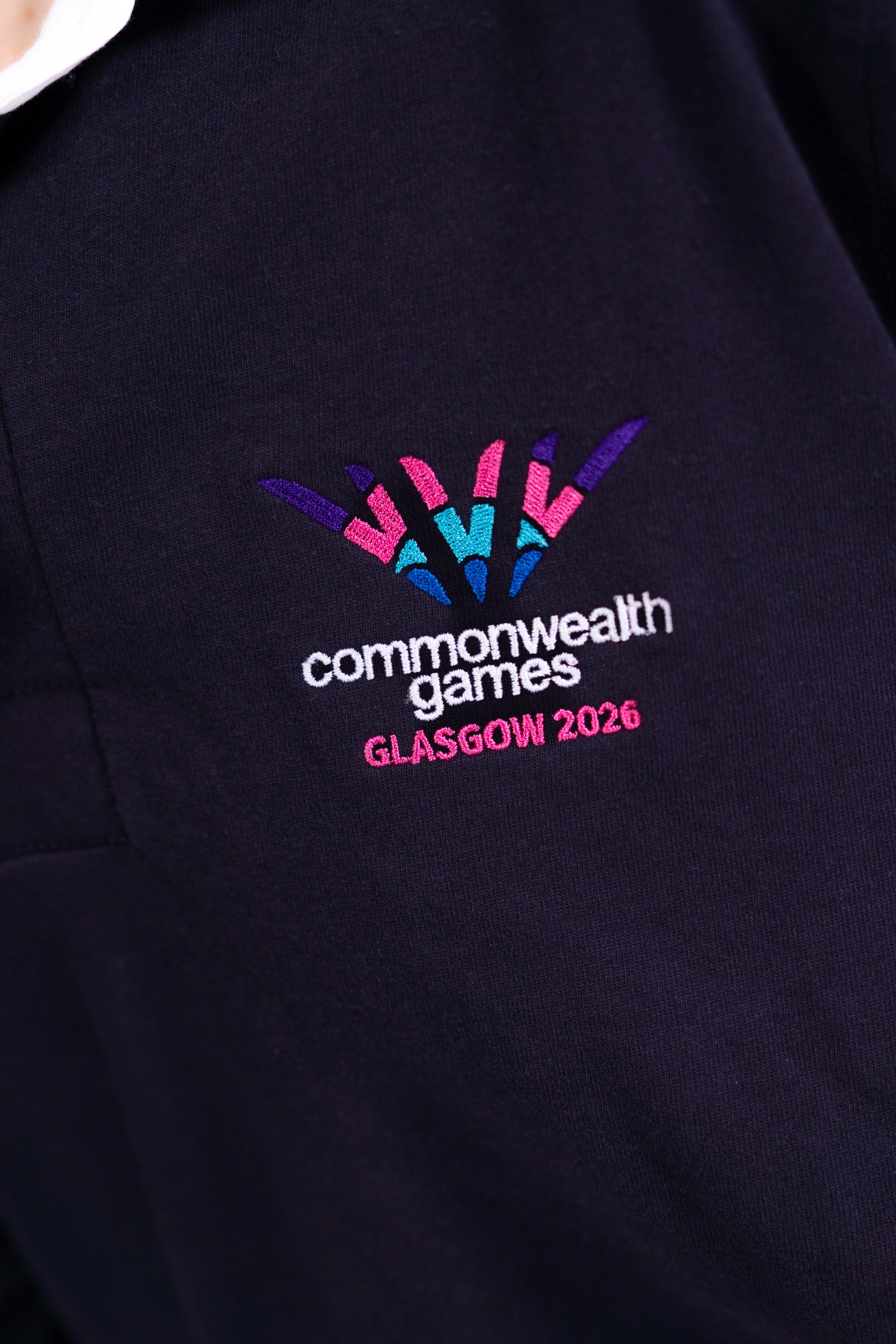 Close up navy Glasgow 2026 logo rugby top with white collar showing logo embroidery.