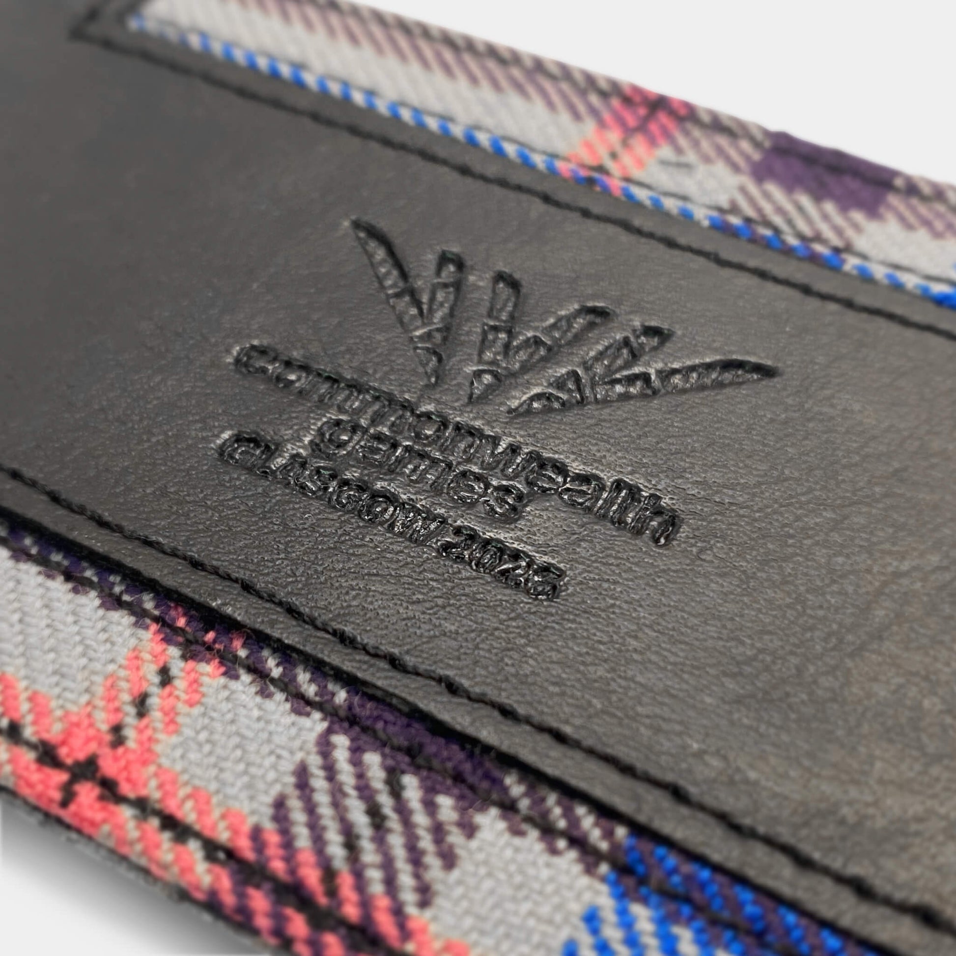 Close up view of Glasgow 2026 Tartan Luggage Tag on grey background showing debossed logo detail