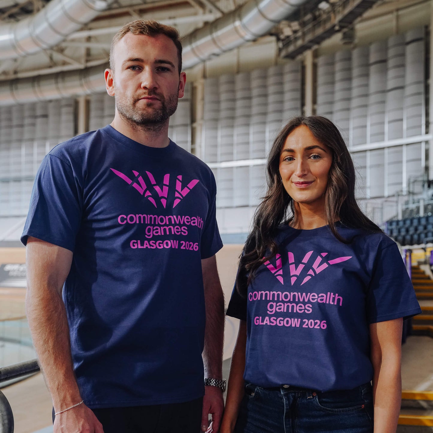 Man and woman both wearing navy single colour Glasgow 2036 logo t-shirts