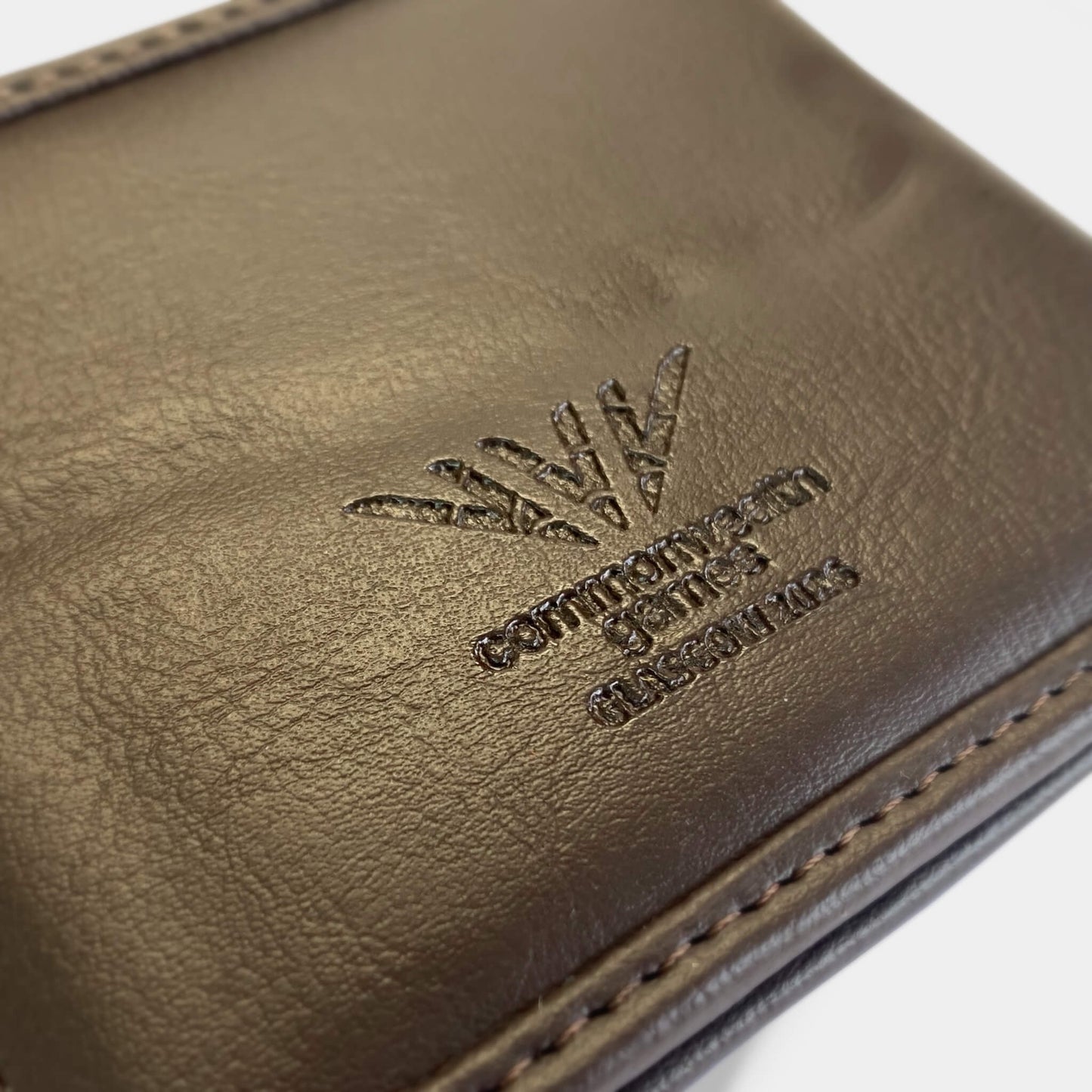 Closeup view of Glasgow 2026 Country Green Harris Tweed Men's Wallet on grey background showing debossed logo detail.